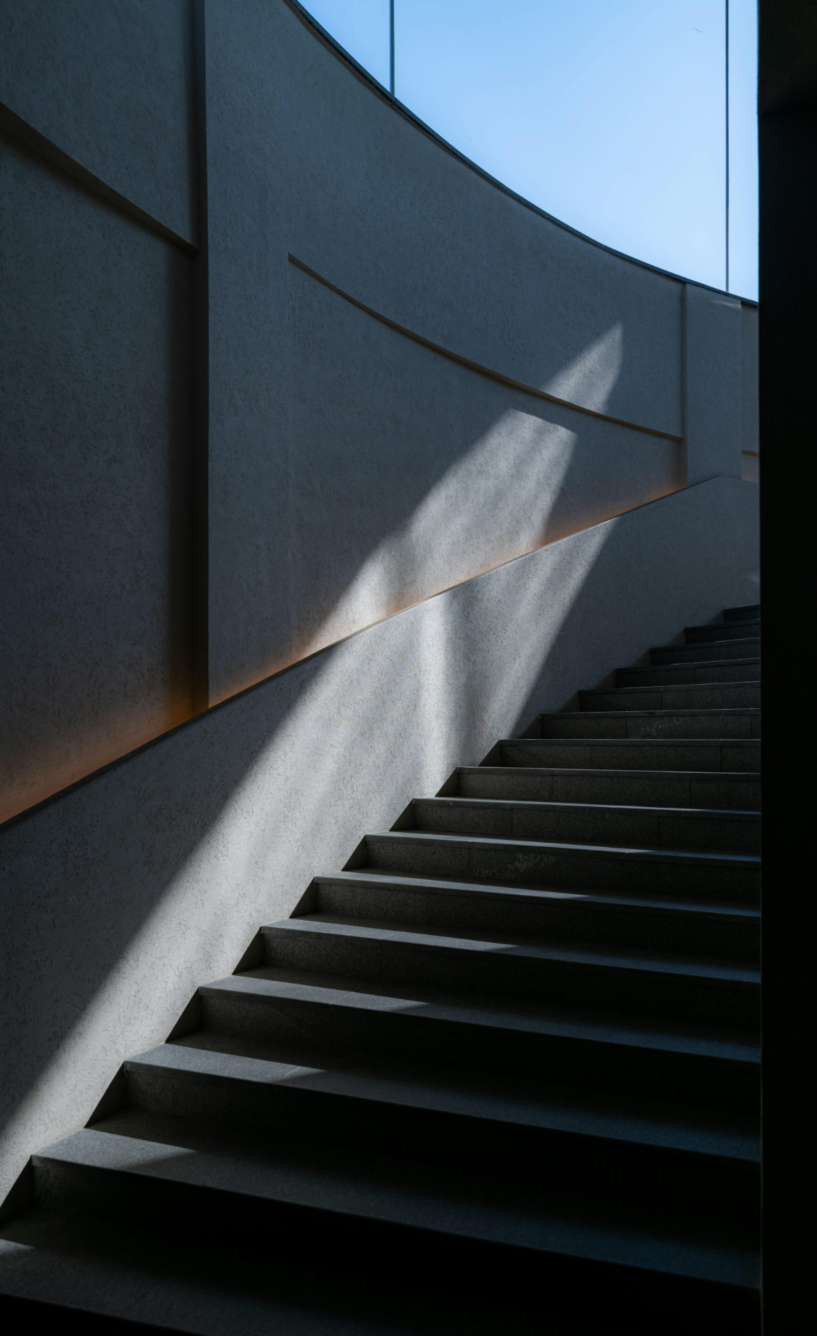 Architectural staircase rising through geometric shadow and daylight